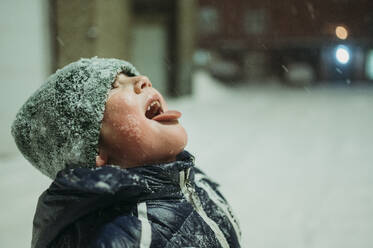 Happy boy catching snow with tongue in winter - ANAF02530