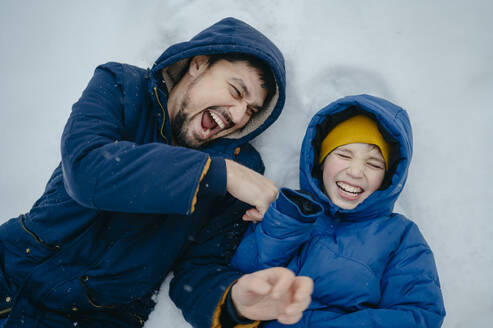 Happy father with son lying on snow and laughing in winter - ANAF02531