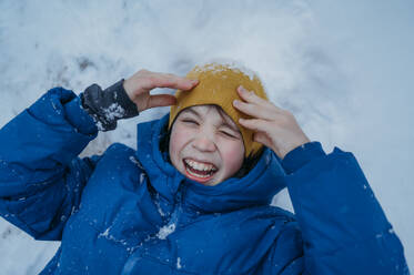 Happy boy lying on snow and laughing in winter - ANAF02532