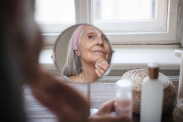 Senior woman making make up herself in home. Skincare routine of beautiful elderly woman. Reflection in the beauty mirror. - HPIF34439
