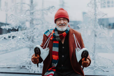 Porträt eines glücklichen älteren Mannes im Winter auf einer Eislaufbahn im Freien. - HPIF34449