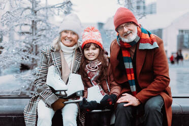 Portrait of seniors and their granddaughter in a winter at outdoor ice skating rink. - HPIF34452