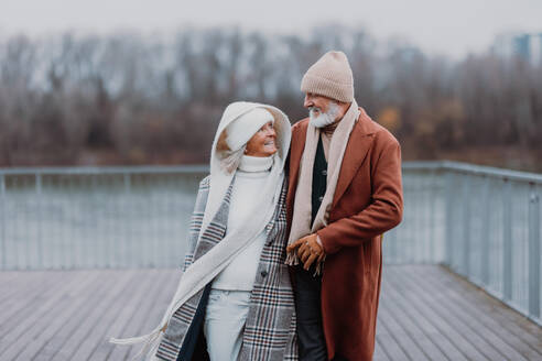 Elegant senior couple walking near a river, during cold winter day. - HPIF34455