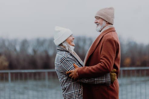 Elegantes älteres Paar, das an einem kalten Wintertag in der Nähe eines Flusses spazieren geht. - HPIF34456