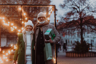 Happy senior couple enjoying outdoor christmas market, buying gifts. - HPIF34461