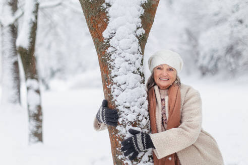 Taille nach oben Porträt der eleganten älteren Frau stehen durch einen Baum, während kalten Winter verschneiten Tag. Ältere Frau verbringen Winterurlaub in den Bergen. Wintry Weihnachten Landschaft. - HPIF34481