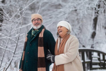 Elegantes älteres Paar, das im verschneiten Park spazieren geht, während eines kalten, verschneiten Wintertages. Älteres Paar, das Winterurlaub in den Bergen verbringt. Winterliche Weihnachtslandschaft. - HPIF34514