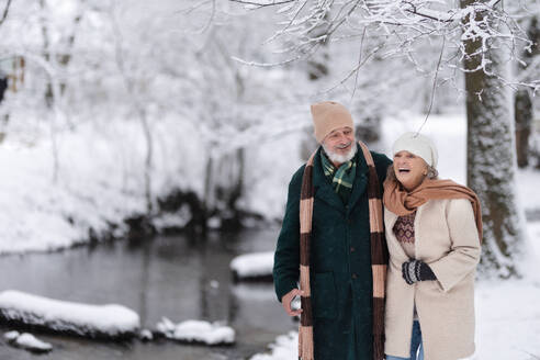 Elegantes älteres Paar, das im verschneiten Park spazieren geht, während eines kalten, verschneiten Wintertages. Älteres Paar, das Winterurlaub in den Bergen verbringt. Winterliche Landschaft. - HPIF34524