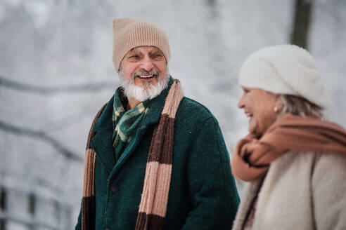 Nahaufnahme eines eleganten älteren Mannes, der mit seiner Frau im verschneiten Park spazieren geht, während eines kalten, verschneiten Wintertages. Älteres Paar, das Winterurlaub in den Bergen verbringt. Winterliche Landschaft. - HPIF34525