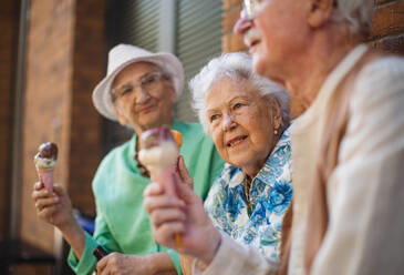 Porträt von drei älteren Freundinnen in der Stadt, die an einem heißen Sommertag Eis essen. Ältere Damen im Sommerurlaub in der Stadt. Rentner auf Gruppenreise. Konzept von Seniorenurlaub und Reisegruppen, Clubs. - HPIF34537