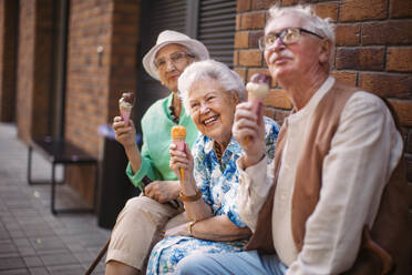 Porträt von drei älteren Freundinnen in der Stadt, die an einem heißen Sommertag Eis essen. Ältere Damen im Sommerurlaub in der Stadt. Rentner auf Gruppenreise. Konzept von Seniorenurlaub und Reisegruppen, Clubs. - HPIF34538