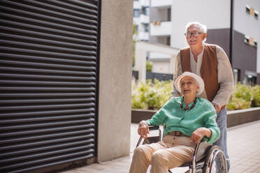 Portrait of senior couple with woman in wheelchair. Elderly man pushing his lovely wife in wheelchair. Concept of chronic illness in elderly couple. Portrait with copy space on black background. Senior siblings on a Sunday stroll in the city. - HPIF34547