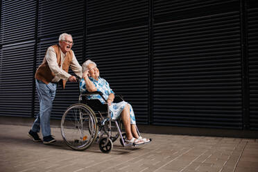 Porträt eines älteren Paares mit Frau im Rollstuhl. Älterer Mann schiebt seine lächelnde Frau im Rollstuhl. Konzept der chronischen Krankheit bei einem älteren Paar. Porträt mit Kopierraum auf schwarzem Hintergrund. - HPIF34549