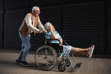 Porträt eines älteren Paares mit Frau im Rollstuhl. Älterer Mann schiebt seine behinderte Frau im Rollstuhl. Konzept der chronischen Krankheit bei einem älteren Paar. Porträt mit Kopierraum auf schwarzem Hintergrund. - HPIF34550