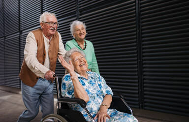 Porträt einer Gruppe älterer Freunde mit einer Frau im Rollstuhl. Ältere Freunde, die eine ältere Frau im Rollstuhl schieben. Konzept der chronischen Krankheit bei einem älteren Paar. Porträt mit Kopierraum auf schwarzem Hintergrund. - HPIF34551