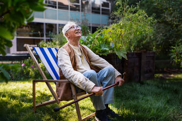 Porträt eines lächelnden älteren Mannes, der sich nach der Pflege von Gemüsepflanzen im städtischen Garten ausruht. Städtische Gartenarbeit im Gemeinschaftsgarten macht einen Rentner glücklich und heilt seine Depression. - HPIF34554