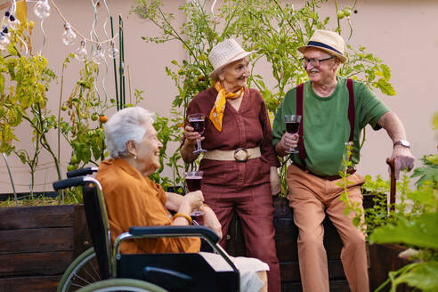 Porträt von älteren Freunden, die sich nach harter Arbeit im städtischen Garten in der Stadt bei einem Glas Wein entspannen. Rentner verbringen ihre Zeit gemeinsam bei der Gartenarbeit im Gemeinschaftsgarten in ihrer Wohnanlage. - HPIF34589