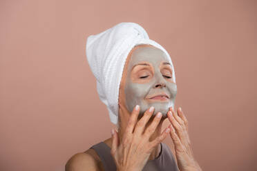Porträt einer aufgeregten älteren Frau mit einer Gesichtsmaske, einem Konzept für Selbstpflege und Hautroutine. - HPIF34618
