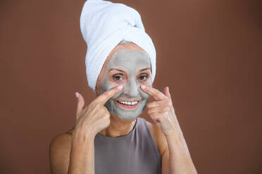Porträt einer aufgeregten älteren Frau mit einer Gesichtsmaske, einem Konzept für Selbstpflege und Hautroutine. - HPIF34621