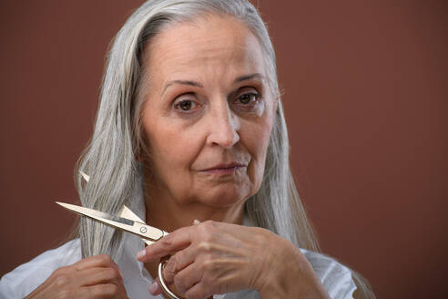 Porträt einer unglücklichen älteren Frau, die sich wegen Brustkrebs die Haare schneidet, Konzept zur Sensibilisierung für Brustkrebs. - HPIF34639