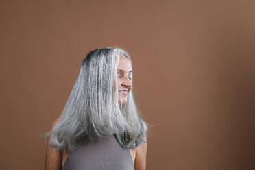 Seitenansicht einer schönen älteren Frau mit langen, dichten, grauen Haaren, isoliert auf einem braun-rosa Hintergrund, Kopierraum. - HPIF34669