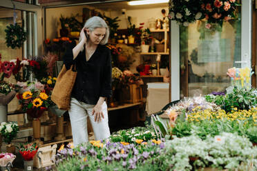 Porträt einer schönen reifen Frau, die auf einem Blumenmarkt in der Stadt einkauft. Frau mittleren Alters kauft frische Blumen, Blumenstrauß von einem Marktstand. - HPIF34730