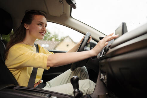 Junge Frau, die den Multimedia-Touchscreen in ihrem Auto berührt. Frau, die ihr Telefon mit dem Auto verbindet. Geschäftsfrau, die das Navigationssystem benutzt, während sie zu einem Treffen fährt. - HPIF34855