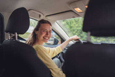 Porträt einer jungen Frau, die auf dem Fahrersitz eines Autos sitzt. Glückliche Frau, die ihr erstes eigenes Auto kauft und fährt. - HPIF34858