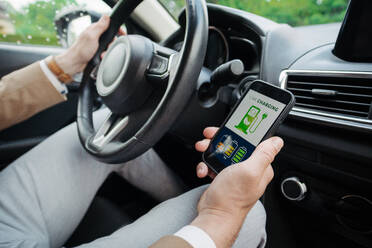 Nahaufnahme eines Geschäftsmannes, der eine App zum Aufladen von Elektrofahrzeugen nutzt, um den Stromverbrauch und die nächstgelegene Ladestation auf seinem Smartphone zu überprüfen. - HPIF34865