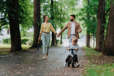 Junge Familie mit kleinem Sohn auf einem Spaziergang in einem Stadtpark nach der Arbeit. Berufstätige Eltern verbringen Zeit mit ihrem Sohn nach dem Arbeitstag. Eltern holen ihr Kind von der Kindertagesstätte ab. - HPIF34882