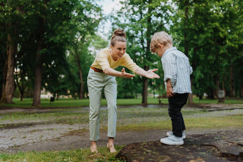 Eine Mutter wartet darauf, ihren verspielten Sohn aufzufangen. Ein kleiner Junge will im Park von einem Baumstumpf springen, seine Mutter fängt ihn auf. - HPIF34885