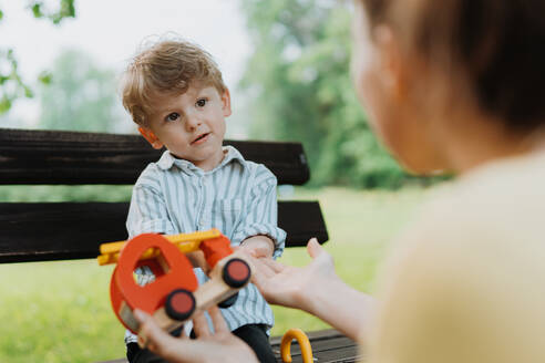 Alleinerziehende Mutter mit kleinem Sohn spielt mit Holzspielzeug auf einer Parkbank. Berufstätige Mutter verbringt Zeit mit ihrem Sohn im Stadtpark nach der Arbeit. - HPIF34892