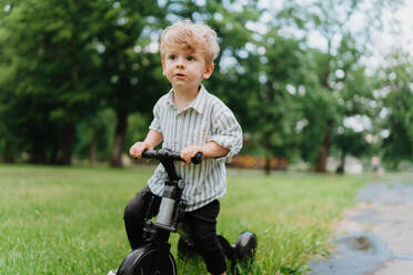 Vorschulkind spielt im Stadtpark, an der frischen Luft, nach Abschluss des Kindergartens. Kleiner süßer Junge fährt mit einem Roller im Park. - HPIF34901