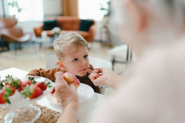 Little boy having sweet snack with his grandmother. Grandmother feeding gradson with donut. - HPIF34920