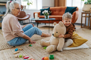 Grandmother playing with her little grandson and teddy bear. Playing with colorful wooden blocks. - HPIF34936