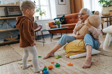 Großmutter spielt mit ihrem kleinen Enkel und einem Spielzeugbären. - HPIF34939