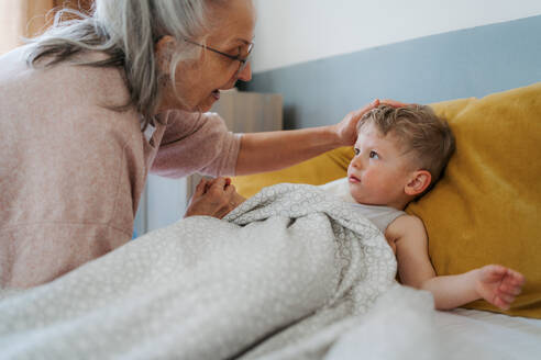 Großmutter, die ihren Enkel in ein Bett legt. - HPIF34941