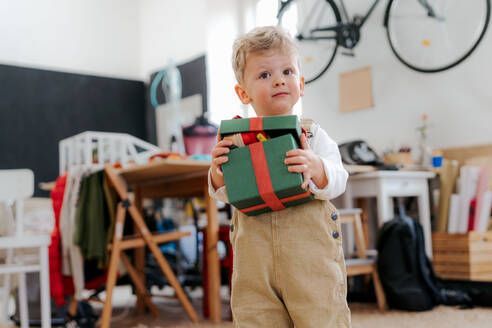 Überraschender kleiner Junge, der ein Geschenk erhält. Glückliches Kind, das ein Geschenkpaket hält und öffnet. - HPIF34943