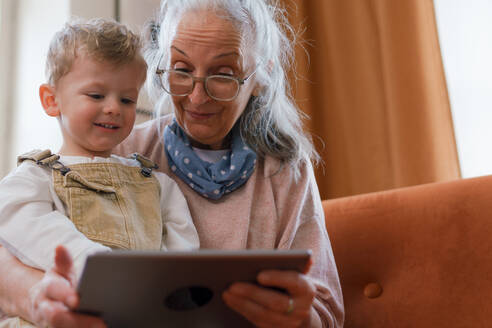 Großmutter, die mit ihrem Enkel auf einem digitalen Tablet ein Märchen anschaut. - HPIF34956