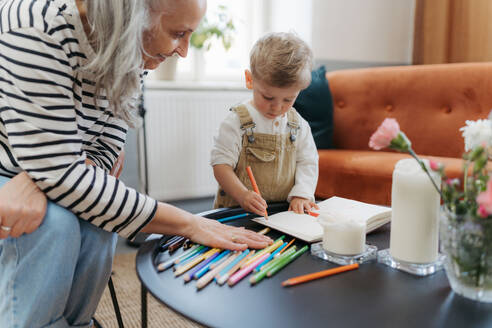 Enkel, der mit seiner Großmutter in einen Notizblock zeichnet. Kleiner Junge, der mit Buntstiften zeichnet. - HPIF35004