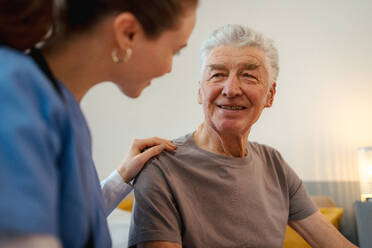 Junge Krankenschwester kümmert sich um einen älteren Menschen in seinem Haus. - HPIF35014