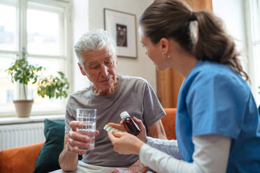 Krankenschwester gibt Tabletten älteren Mann in seiner Wohnung. - HPIF35024