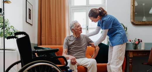 Young nurse helping senior man to stand up from a sofa. - HPIF35027