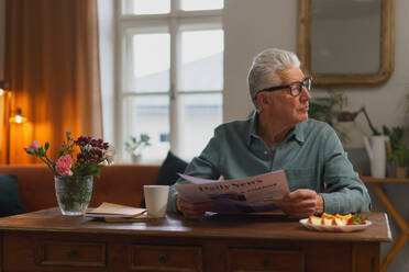 Älterer Mann liest Zeitung in der Wohnung. - HPIF35055