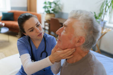 Ein Arzt untersucht die Lymphknoten am Hals, eine junge Krankenschwester kümmert sich um einen älteren Menschen in seinem Haus. - HPIF35059