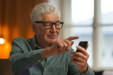 Senior man scrolling his smartphone at his home. - HPIF35091