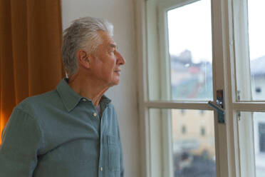 Porträt eines gut aussehenden älteren Mannes mit grauem Haar, der aus dem Fenster schaut, Konzept der Einsamkeit im Ruhestand. - HPIF35095