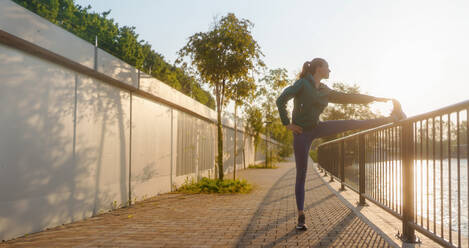 Athletische junge Frau in Sportkleidung macht Dehnübungen vor dem Morgenlauf. Fitness-Mädchen bereitet sich auf das Abendtraining vor. Outdoor-Workout-Konzept. - HPIF35099