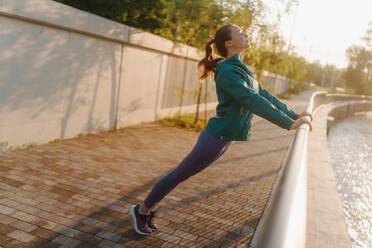 Junge Läuferin streckt die Arme vor ihrem Morgenlauf. Fitness-Mädchen in Sportkleidung bereitet sich auf das Abendtraining vor. Outdoor-Workout-Konzept. - HPIF35102