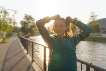Portrait of young female runner doing workout hairstyle before her early morning run. Fitness girl in sportswear preparing for evening exercise. Outdoor workout concept. - HPIF35112